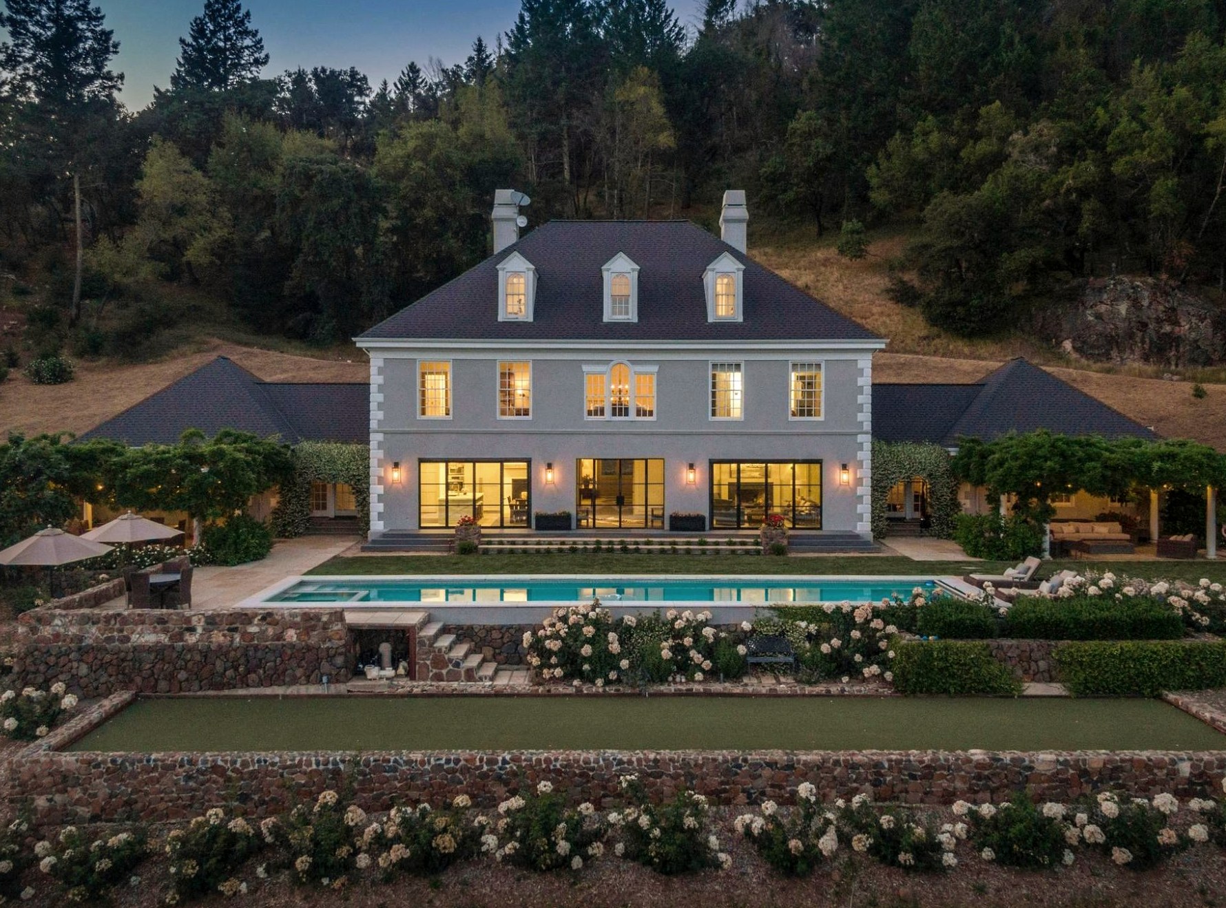 The main house at twilight, lit interior, pool and gardens in foreground